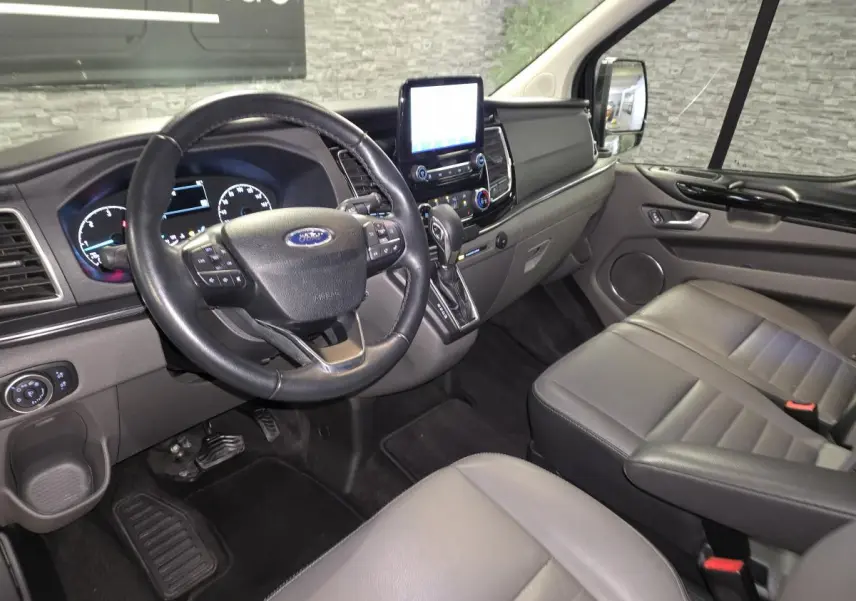 Vue intérieure côté conducteur du Ford Transit Custom noir, montrant le volant cuir, tableau de bord et sièges gris anthracite.