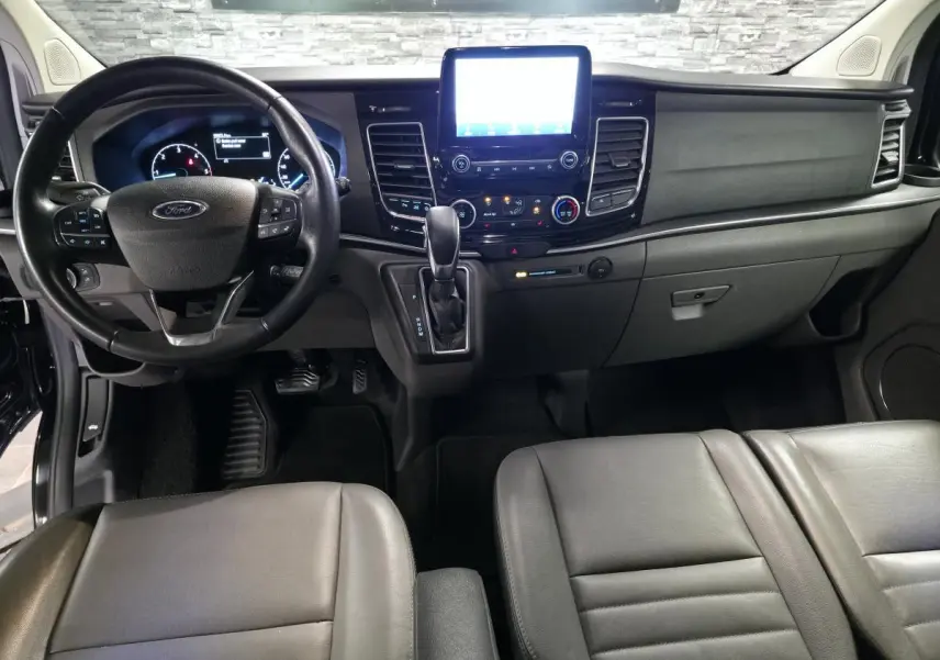 Vue intérieure avant du Ford Transit Custom noir 2022, tableau de bord avec écran tactile et sièges cuir gris anthracite.