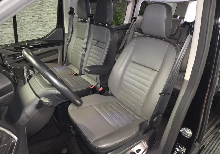 Vue intérieure côté conducteur du Ford Transit Custom noir, sièges en cuir gris anthracite avec accoudoirs et réglages électriques.