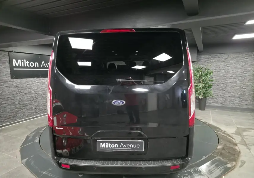 Vue arrière d'un Ford Transit Fourgon Custom noir, avec hayon vitré et feux verticaux intégrés.