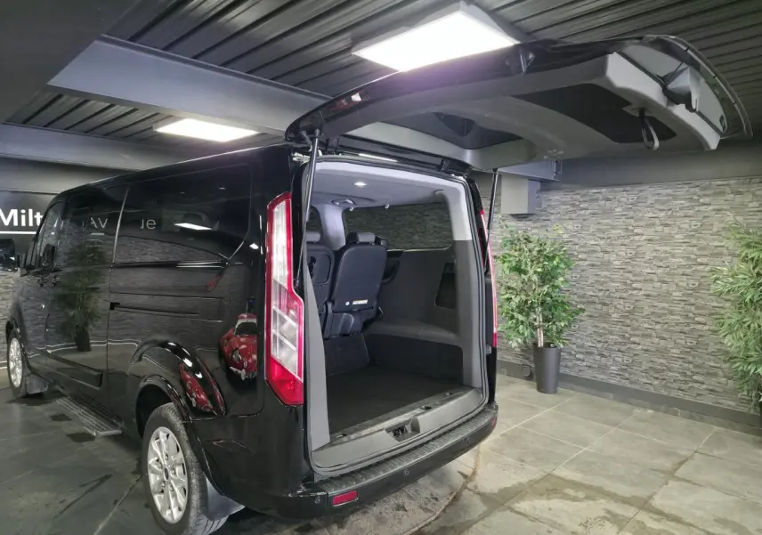 Vue 3/4 arrière droite d’un Ford Transit Fourgon Custom noir avec hayon ouvert montrant l’espace de chargement intérieur.