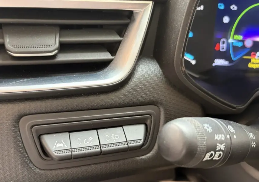 Gros plan sur les commandes d’aide à la conduite et réglage des phares dans l’habitacle d’une Renault Clio blanche hybride 2022.