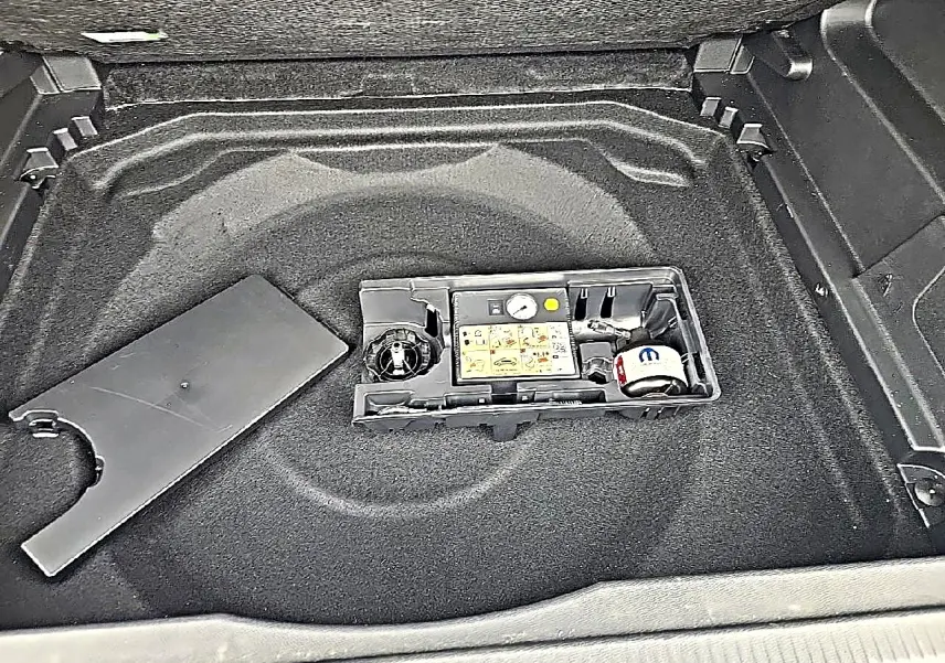 Vue plongeante sur le coffre gris du Citroën C5 Aircross 2025, montrant le rangement sous plancher avec kit de réparation pneus.