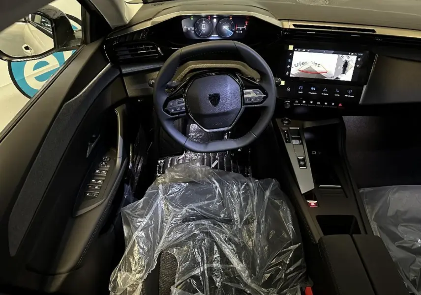 Vue intérieure avant de la Peugeot 308 2024 blanc okenite, volant compact, tableau de bord numérique et écran central tactile allumé.