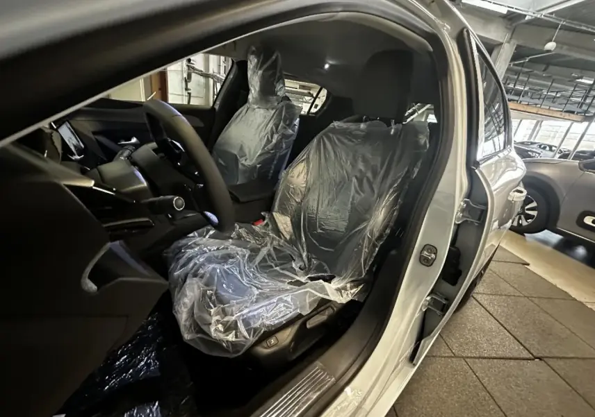 Intérieur de la Peugeot 308 blanc okenite 2024, vue côté conducteur avec sièges avant protégés par film plastique.