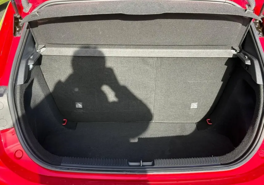 Coffre ouvert vu de face d’une MG3 1.5 Hybrid+ 195ch Luxury en rouge métallisé, intérieur noir et tapis propre.