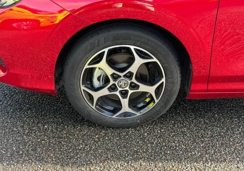 Gros plan sur la roue avant gauche d'une MG3 1.5 Hybrid+ Luxury 2025 en rouge métallisé avec jante alu bicolore.