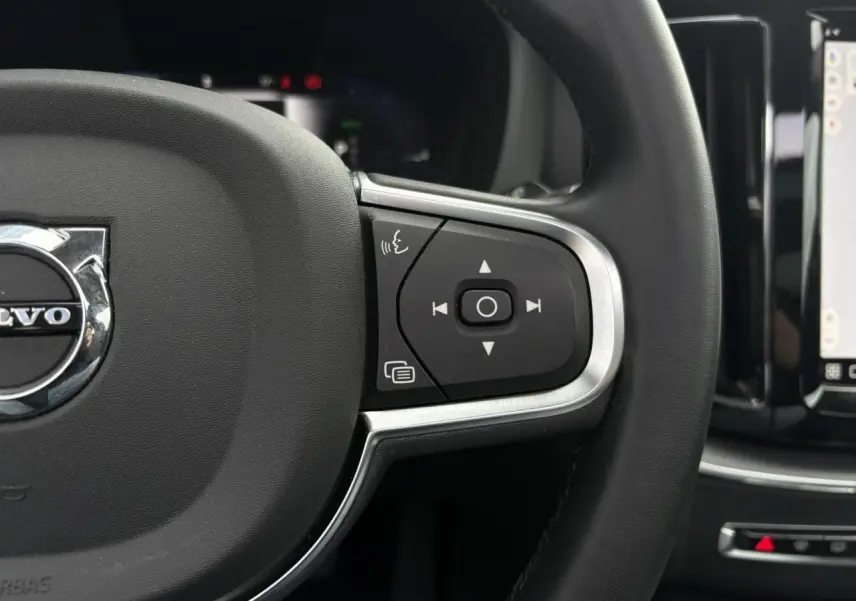 Gros plan sur le volant simili-cuir noir du Volvo XC60 2024 avec commandes audio et écran tactile visible à droite