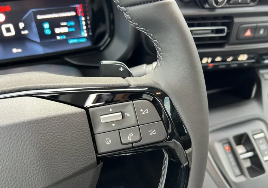 Détail des commandes au volant du Citroën Berlingo 2025 noir perla nera, avec tableau de bord numérique en arrière-plan.