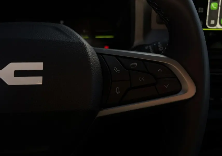 Gros plan sur les commandes multifonctions à droite du volant du Dacia Duster blanc Glacier, intérieur sombre.