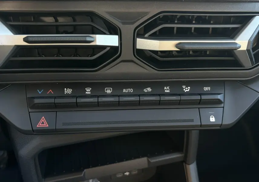 Gros plan sur la console centrale du Dacia Duster blanc Glacier, montrant les commandes de climatisation et les aérateurs noirs.