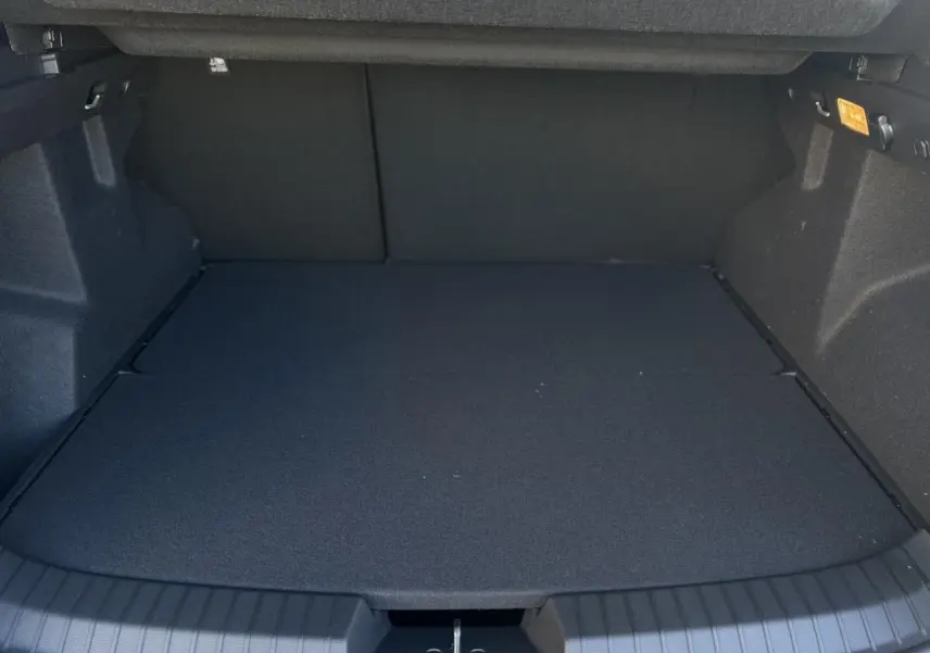 Coffre spacieux du Dacia Duster blanc Glacier 2025, vue intérieure arrière avec plancher plat et revêtement noir.