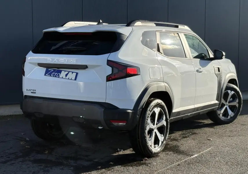 Vue 3/4 arrière droite du Dacia Duster blanc Glacier 2025 avec jantes alliage diamantées et barres de toit noires.