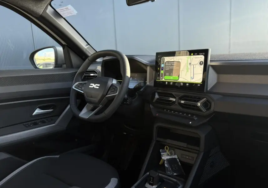 Vue intérieure côté conducteur du Dacia Duster 2025 avec tableau de bord digital et écran tactile central.