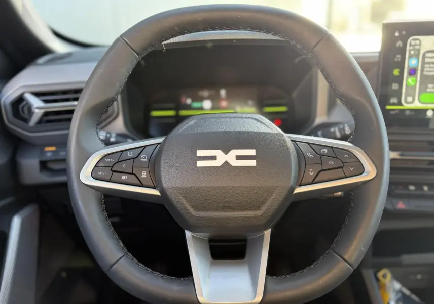 Gros plan sur le volant noir du Dacia Duster 2025 avec commandes intégrées et tableau de bord digital en arrière-plan.