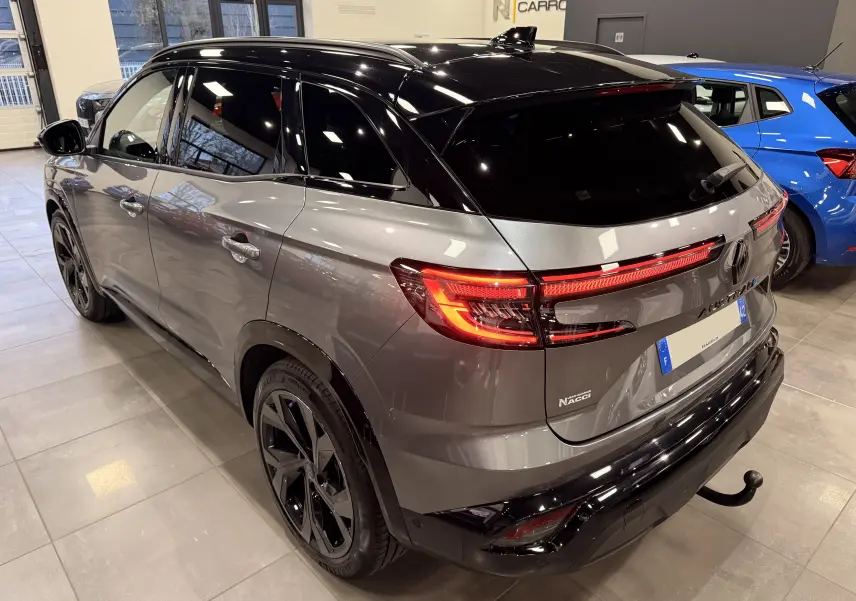 Vue 3/4 arrière droite du Renault Austral gris schist avec toit noir, feux LED allumés et attelage visible en intérieur showroom.