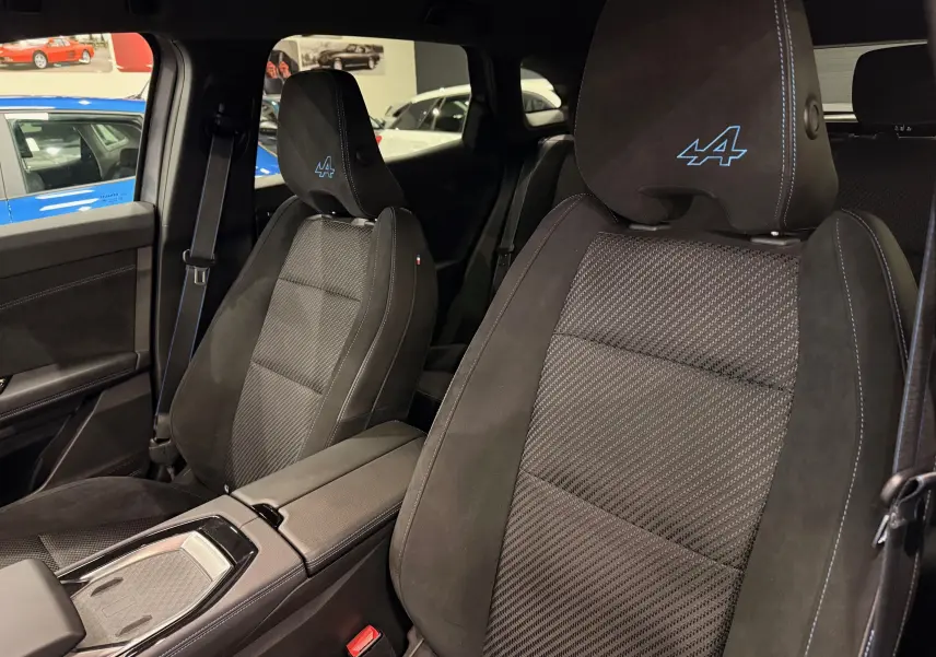 Vue intérieure rapprochée des sièges avant noirs avec surpiqûres bleues et logo Alpine brodé sur les appuie-têtes.