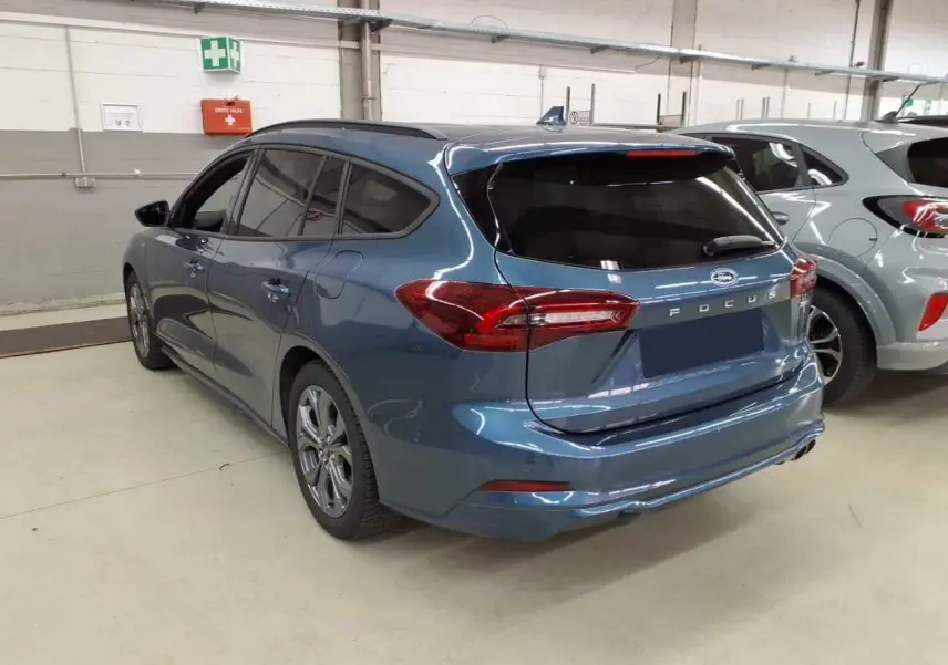 Vue 3/4 arrière droite d'une Ford Focus SW 2023 bleu azur avec attelage et vitres arrière surteintées en intérieur d'atelier.