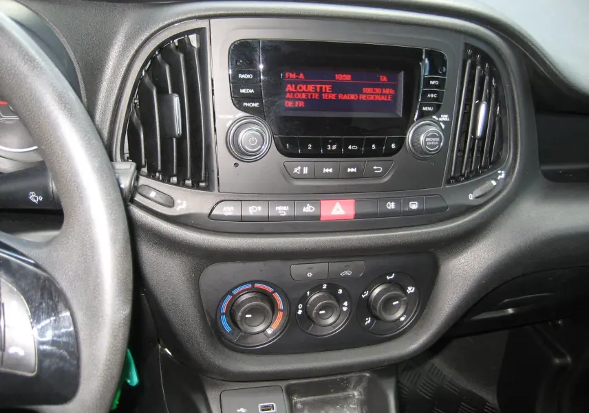 Vue rapprochée du tableau de bord noir du Fiat Doblo Cargo 2018, avec commandes radio et climatisation visibles.