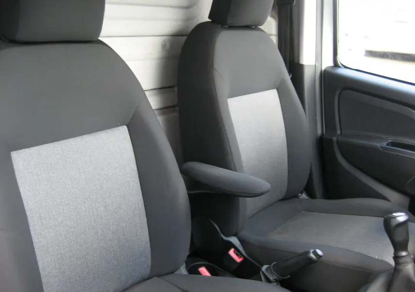 Vue intérieure des sièges avant gris et noir du Fiat Doblo Cargo 2018, avec accoudoir central et levier de vitesses manuel visible.