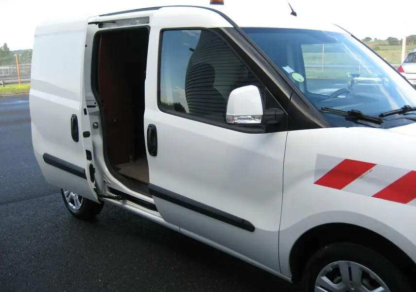 Vue de côté droit d'un FIAT Doblo Cargo blanc 2018 avec porte coulissante ouverte et bande réfléchissante rouge sur l'aile avant.