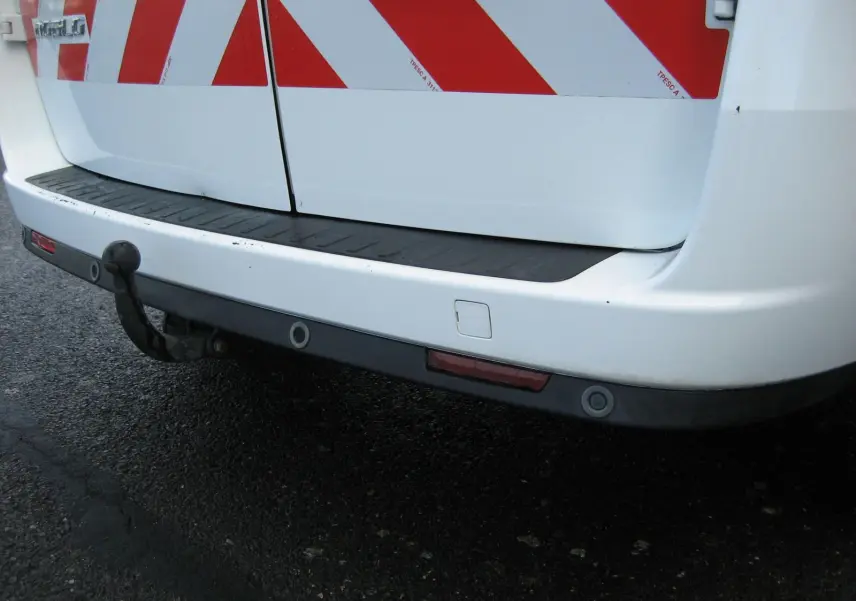 Gros plan sur le pare-chocs arrière blanc du Fiat Doblo Cargo avec attelage et bandes réfléchissantes rouges.