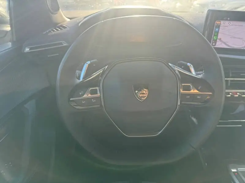 Vue rapprochée du volant noir du Peugeot 2008 Hybrid 136 e-DCS6 Allure avec commandes intégrées et écran tactile visible.