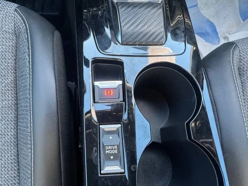Gros plan sur la console centrale noire brillante du Peugeot 2008 Hybrid avec frein à main électrique et bouton Drive Mode.