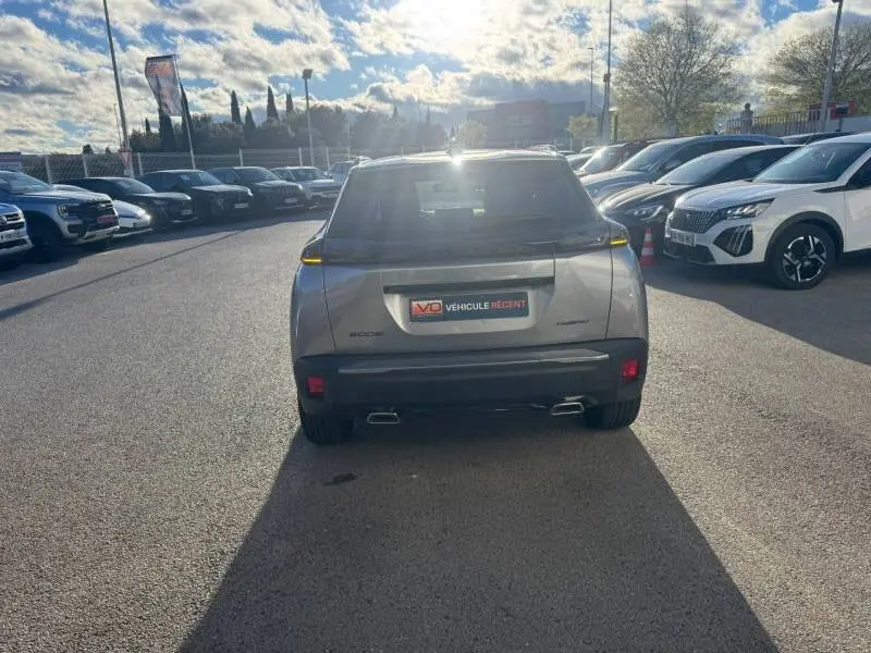 Vue arrière d’un Peugeot 2008 Hybrid gris 2025 avec barres de toit et jantes alliage 17 pouces, en extérieur sous un ciel partiellement nuageux.