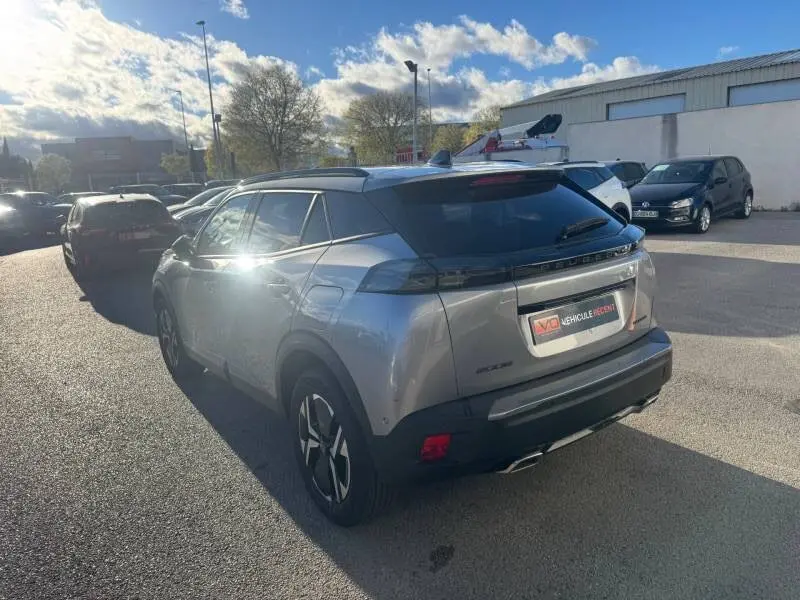 Vue 3/4 arrière droite d'un Peugeot 2008 Hybrid gris 2025 avec barres de toit et jantes alliage 17 pouces.