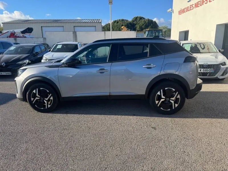 Profil droit d’un Peugeot 2008 Hybrid gris 2025 avec jantes alliage 17 pouces et barres de toit noires.