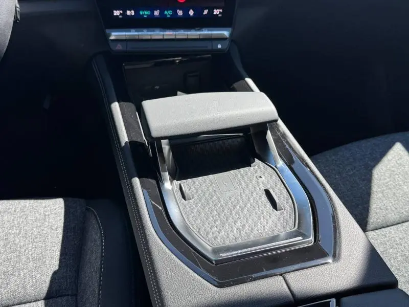 Gros plan sur la console centrale avec accoudoir et zone de recharge sans fil du Renault Austral blanc nacré 2025.