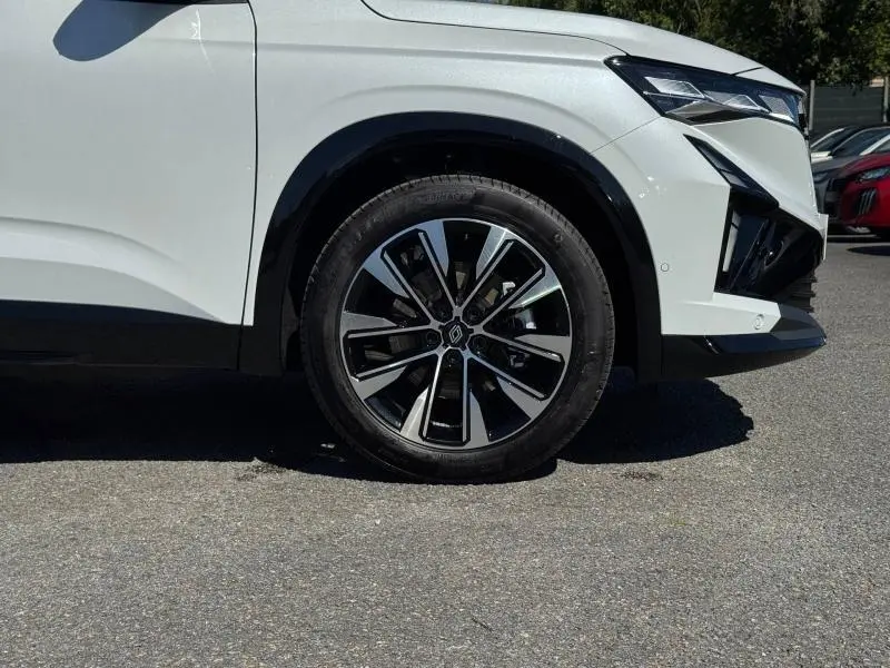 Gros plan sur la roue avant droite et partie avant d’un Renault Austral blanc nacré avec jante alu noire et argent.