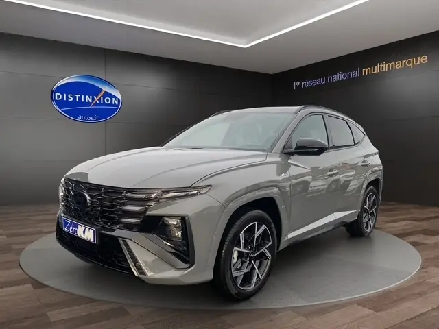 Vue 3/4 avant d'un Hyundai Tucson gris foncé avec jantes alliage et calandre imposante en showroom.