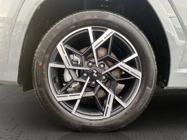 Gros plan sur la roue avant droite du Hyundai Tucson gris foncé, jante alliage noire et argentée au design géométrique.