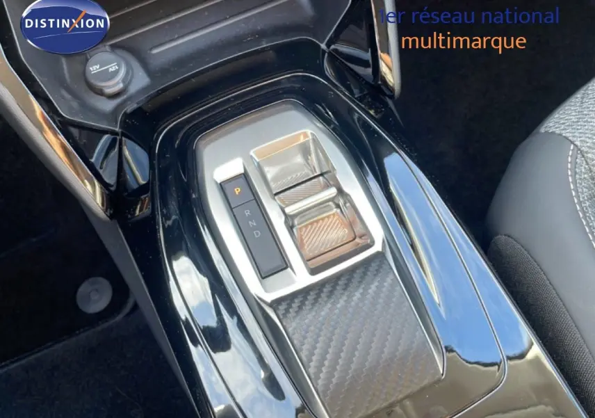 Gros plan sur la console centrale noire brillante de la Peugeot 208 Hybrid 110ch, avec levier de boîte automatique et finition carbone.