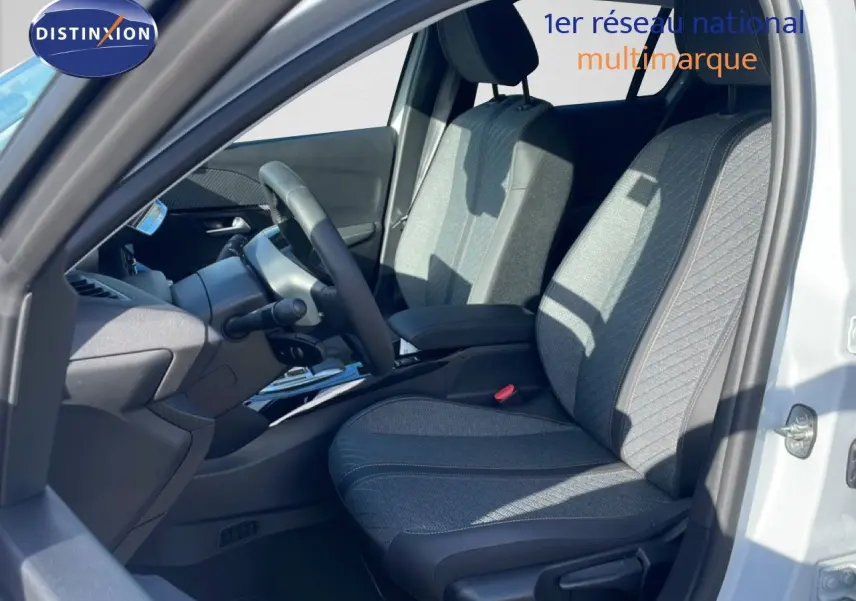 Vue intérieure côté conducteur d'une Peugeot 208 Hybrid blanche, sièges tissu gris avec détails noirs et volant multifonction.