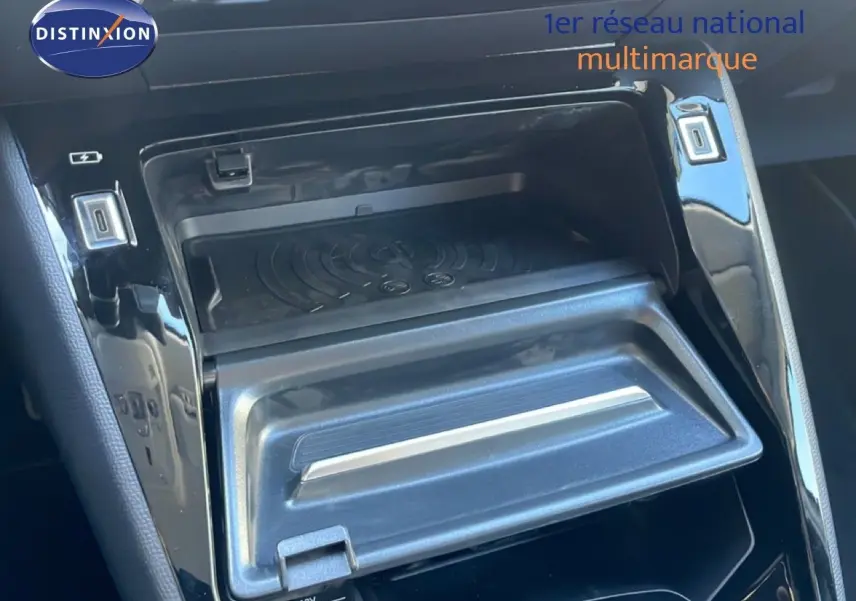 Gros plan sur la console centrale noire de la Peugeot 208 Hybrid 110ch, montrant un compartiment de rangement ouvert avec ports USB.
