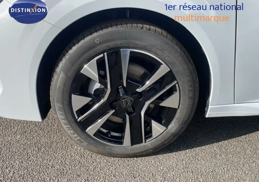 Gros plan sur la roue avant gauche de la Peugeot 208 blanche, mettant en valeur la jante noire et argent au design moderne.