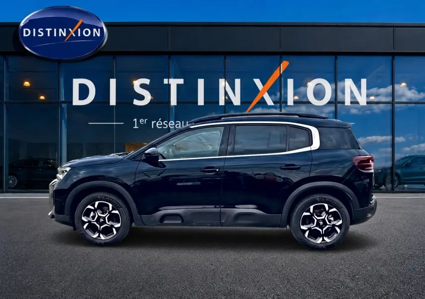 Profil côté gauche du Citroën C5 Aircross noir 2025 avec jantes alu et barres de toit visibles devant une vitrine Distinxion.