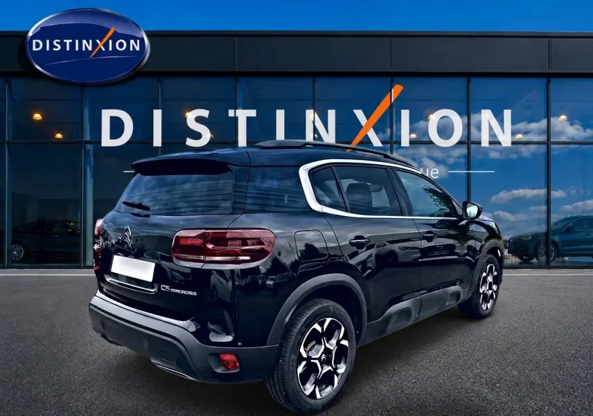Vue 3/4 arrière droite d'un Citroën C5 Aircross noir avec jantes alu et barres de toit visibles devant un bâtiment.