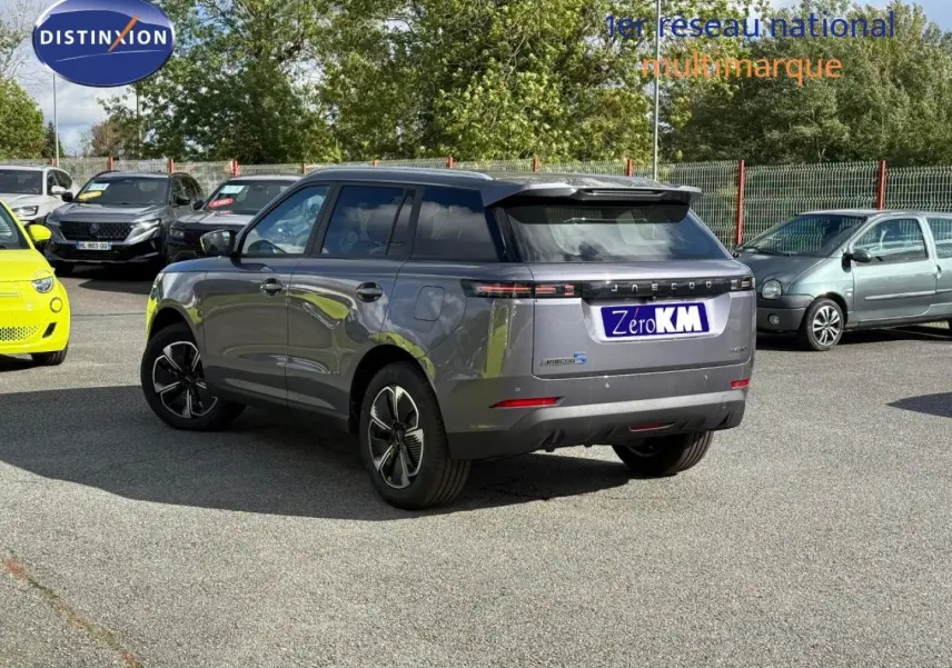 Vue 3/4 arrière droite du JAECOO J5 Phantom Grey métal avec jantes alu et toit noir dans un parking extérieur.