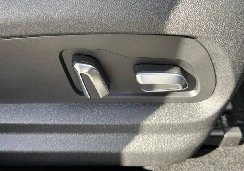 Détail des commandes électriques de réglage du siège avant en plastique noir avec boutons argentés.
