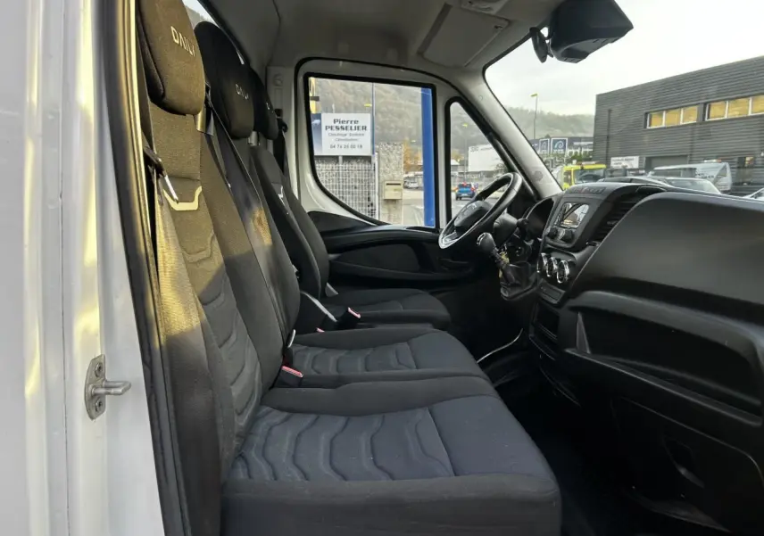 Intérieur du Iveco Daily blanc vu côté gauche, montrant les sièges noirs et le tableau de bord avec volant et levier de vitesses.