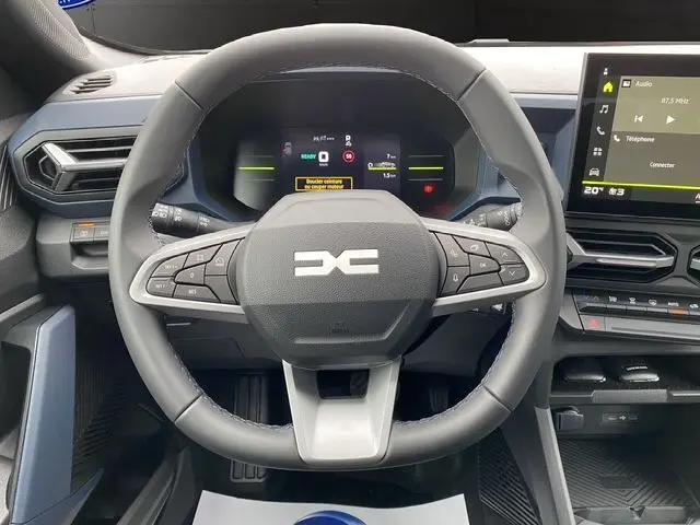 Vue rapprochée du volant multifonction gris du Dacia Duster 1.6 Hybrid 140 Journey 2025 avec tableau de bord numérique et écran tactile.