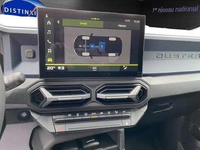 Tableau de bord du Dacia Duster 2025 gris schiste, avec écran tactile affichant l'énergie hybride et aérateurs hexagonaux.