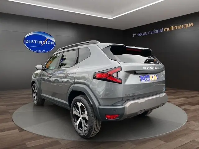 Vue 3/4 arrière droite du Dacia Duster 1.6 Hybrid 140 gris schiste avec jantes alliage et toit noir en showroom.
