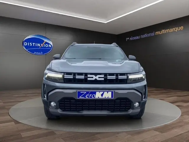 Vue frontale du Dacia Duster 1.6 Hybrid 140 gris schiste avec éclairage LED et calandre distinctive dans un showroom.