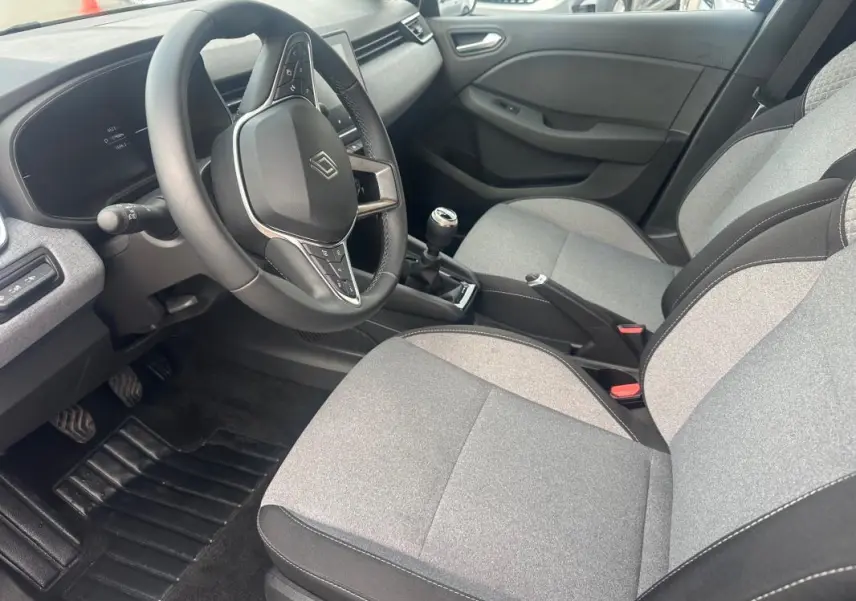 Vue intérieure côté conducteur de la Renault Clio V dCi 100 Evolution 2025, montrant le volant, la boîte manuelle et les sièges gris.