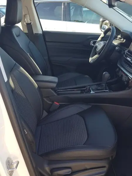 Intérieur du Jeep Compass 2024 blanc vu côté conducteur, sièges noirs avec accoudoir central et tableau de bord moderne.